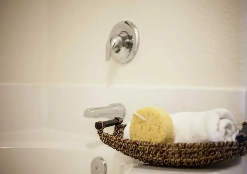 Driftwood stage model home bathroom with wicker tray that has yellow sponge and white towel in it sitting on the side of the bathtub Driftwood stage model home bathroom with wicker tray that has yellow sponge and white towel in it sitting on the side of the bathtub