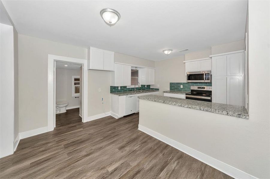 Kitchen featuring a sink, white cabinets, appliances with stainless steel finishes, decorative backsplash, and dark wood-style floors