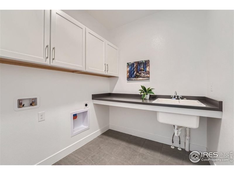 Upper level laundry with added storage, tile flooring and a utility sink.