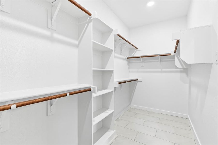 Walk-in closet featuring built-in shelving, multiple hanging rods, and light-toned tile flooring