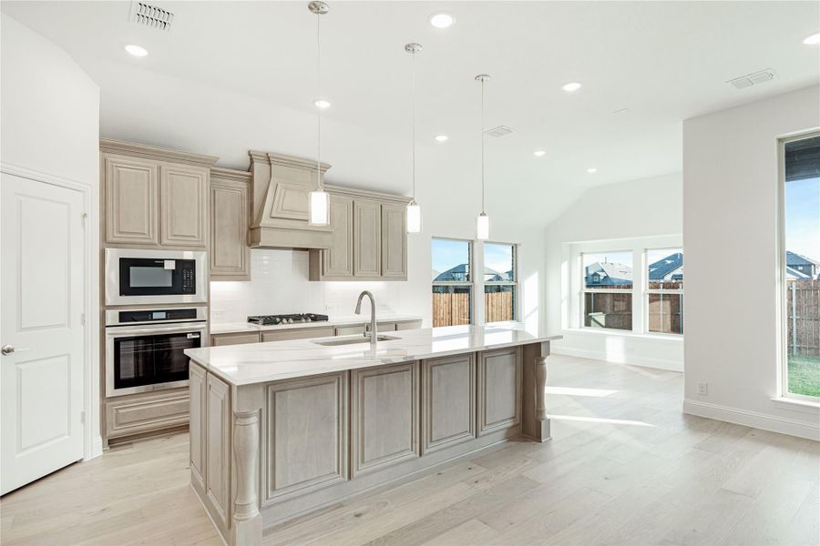 Kitchen with large center island, gray cabinets, stainless steel appliances, and light hardwood floors open to living area