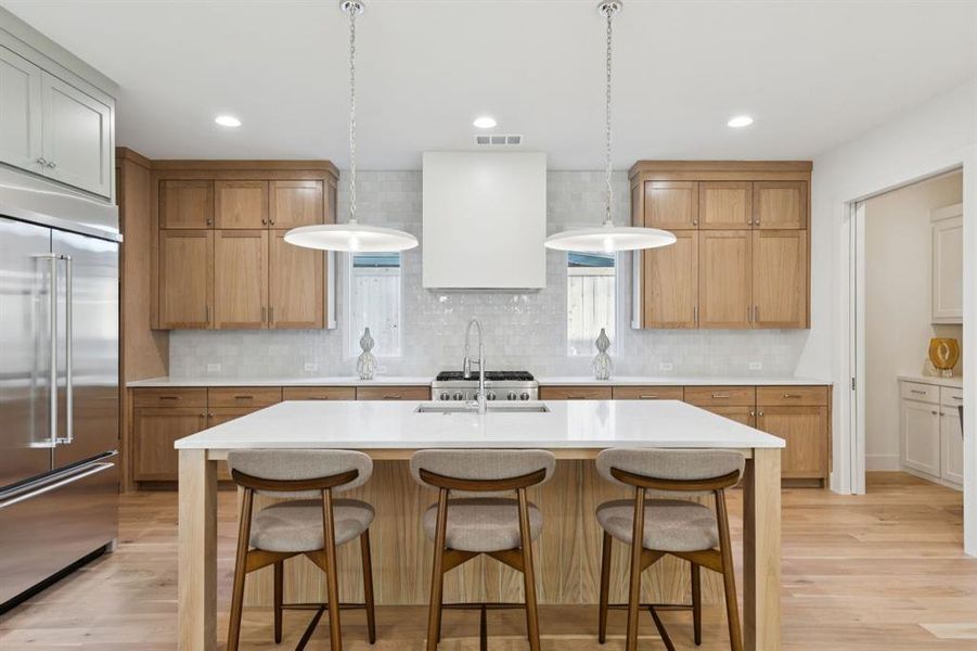 Kitchen with a breakfast bar, light countertops, built in fridge, a center island with sink, and recessed lighting