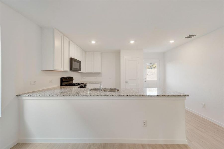 Kitchen with sink, white cabinetry, light stone counters, kitchen peninsula, and black appliances