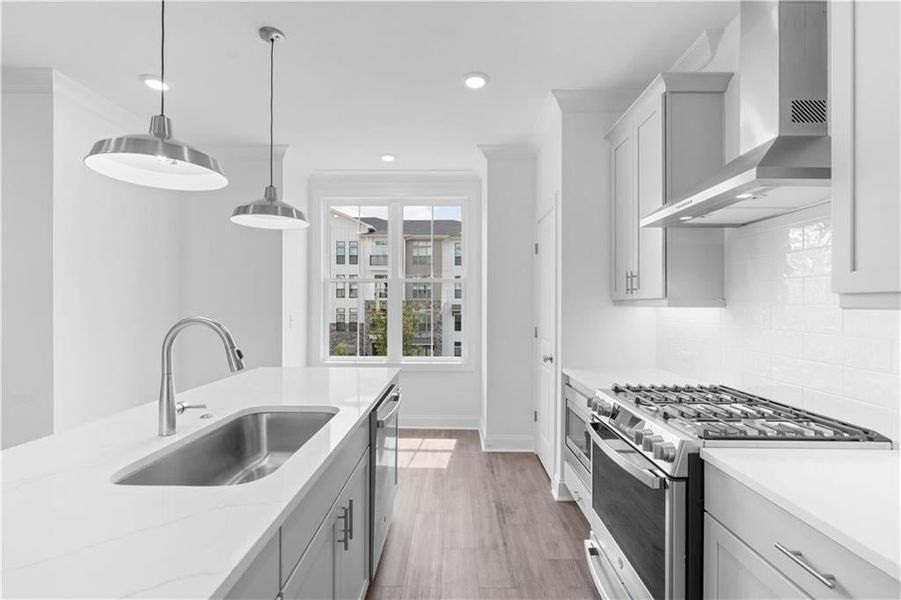 Kitchen featuring appliances with stainless steel finishes, wall chimney exhaust hood, decorative light fixtures, backsplash, and light stone countertops