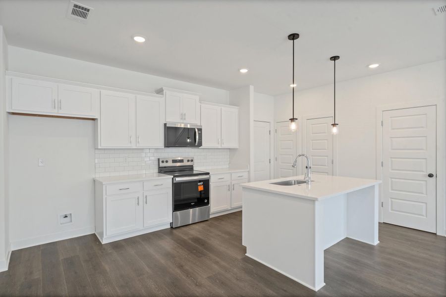 Modern kitchen featuring white cabinetry, subway tile backsplash, stainless steel appliances, and a central island with a sink and pendant lighting