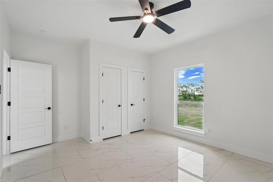 Unfurnished bedroom with light marble finish floors, baseboards, and ceiling fan Unfurnished bedroom with light marble finish floors, baseboards, and ceiling fan