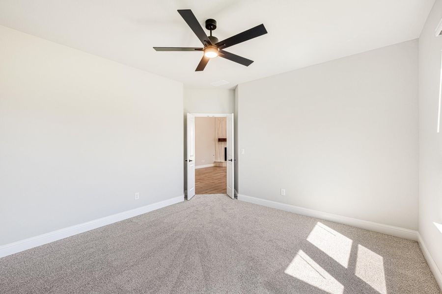 Empty bedroom with gray carpet, white walls, black ceiling fan, and open door to ensuite bathroom Empty bedroom with gray carpet, white walls, black ceiling fan, and open door to ensuite bathroom
