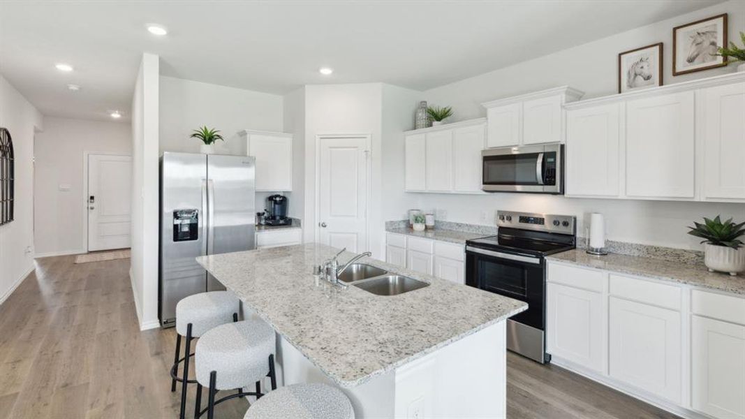 Kitchen with stainless steel appliances, light wood-type flooring, a kitchen breakfast bar, white cabinetry, and light stone countertops