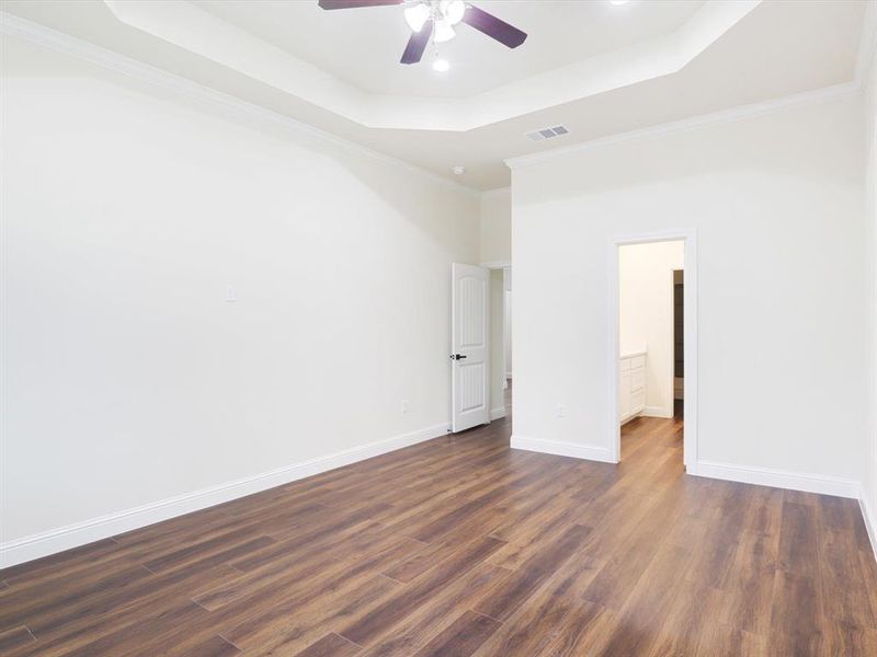 Unfurnished bedroom with crown molding, ceiling fan, dark wood-type flooring, and a raised ceiling Unfurnished bedroom with crown molding, ceiling fan, dark wood-type flooring, and a raised ceiling