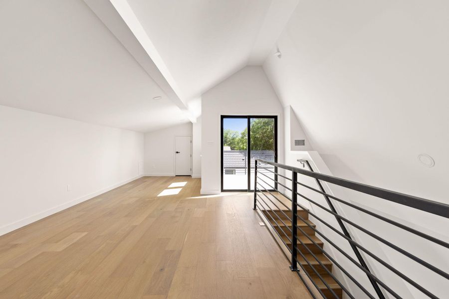 A spacious upper-level area offers hardwood floors, abundant natural light, and modern railing overlooking the staircase.