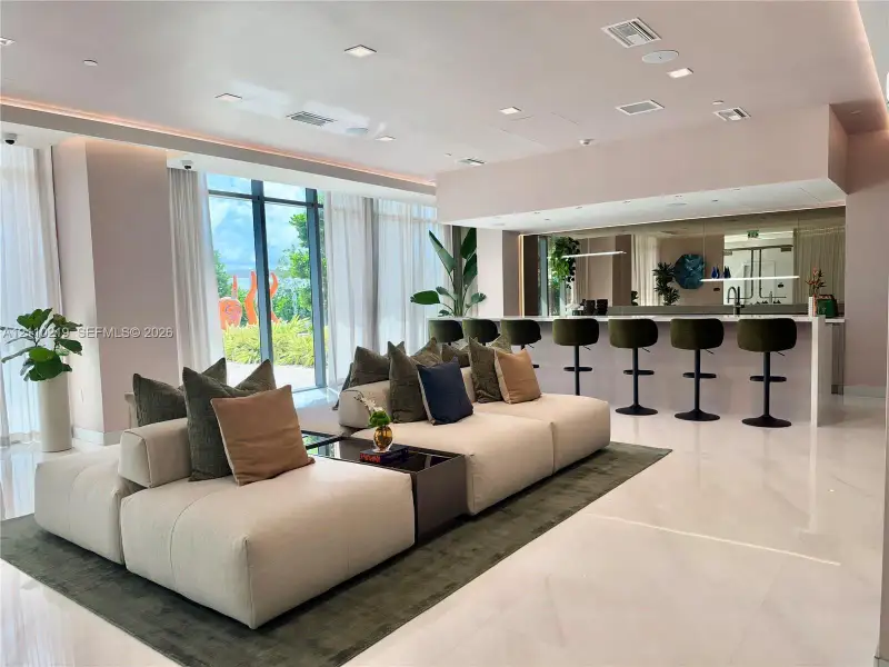 Open-concept interior featuring polished stone flooring, floor-to-ceiling windows, recessed lighting, and a built-in bar with mirror backsplash