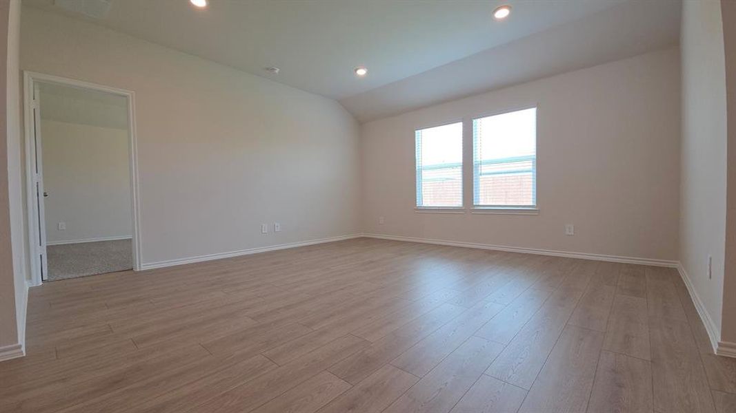 Spacious interior room featuring light wood-finish flooring, recessed lighting, and two windows with white blinds