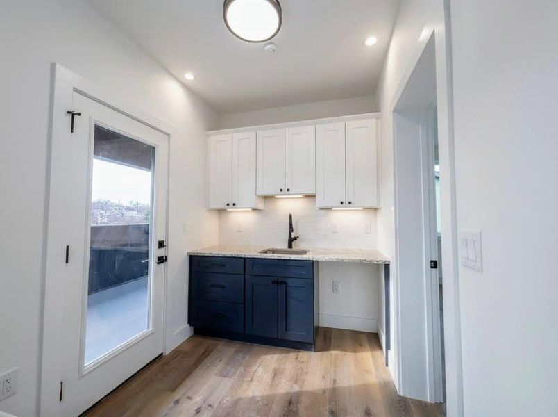 Bar featuring two tone cabinetry, light wood-type flooring, light stone counters, recessed lighting, and backsplash
