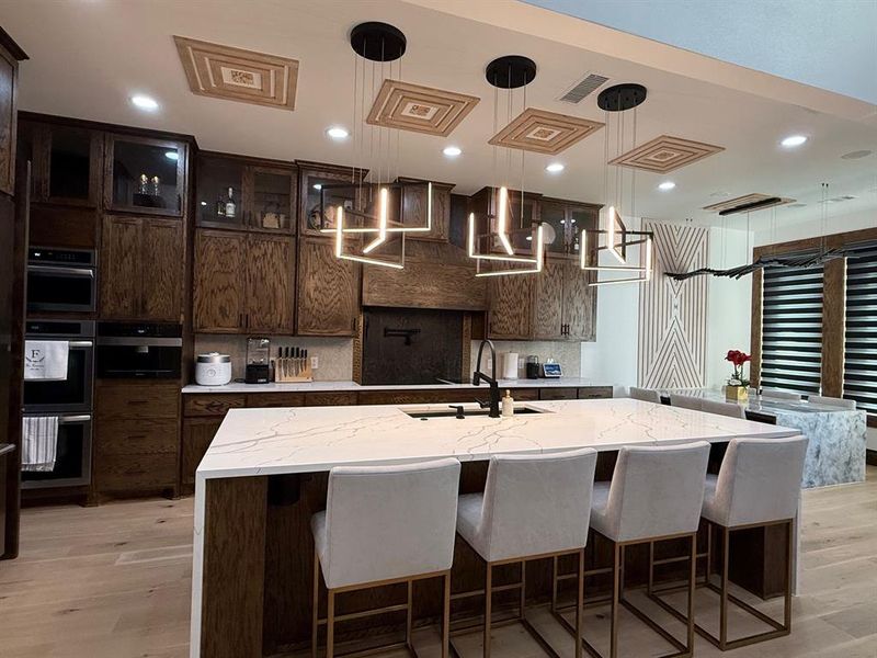 Kitchen featuring a kitchen bar, light stone countertops, dark brown cabinetry, glass insert cabinets, and light wood-style flooring