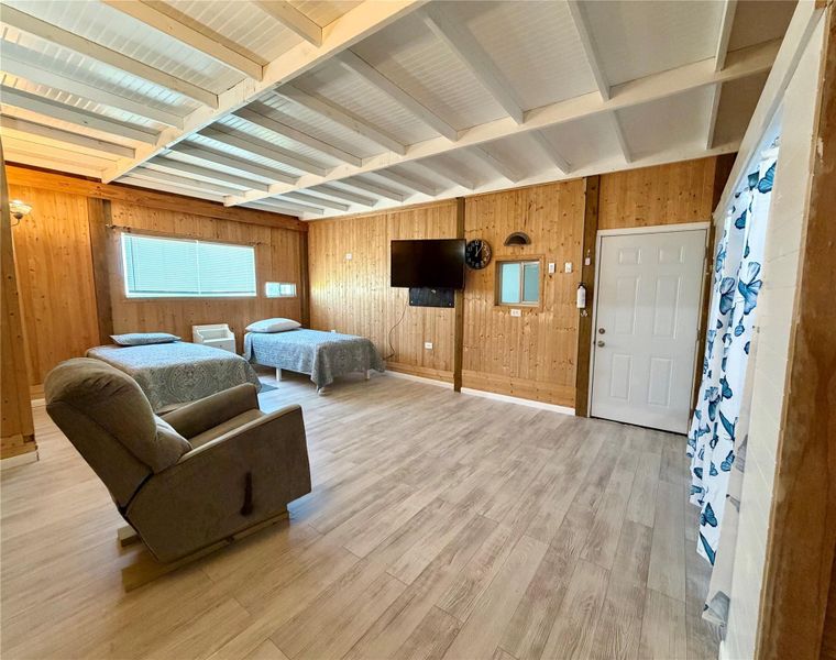 A spacious, naturally illuminated room features light wood paneling, exposed beam ceilings, and durable plank flooring.