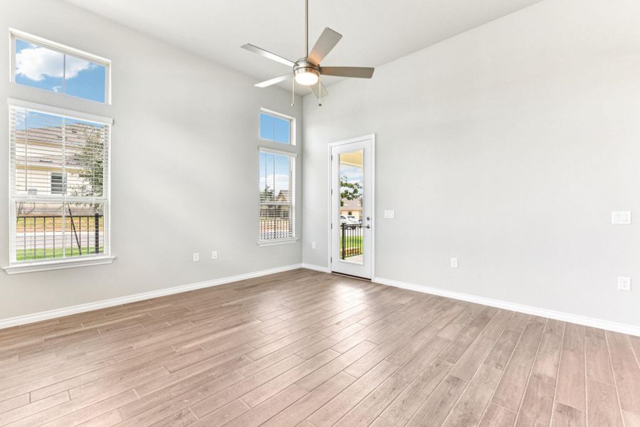 Empty room featuring healthy amount of natural light, a high ceiling, light wood-style floors, and a ceiling fan Empty room featuring healthy amount of natural light, a high ceiling, light wood-style floors, and a ceiling fan