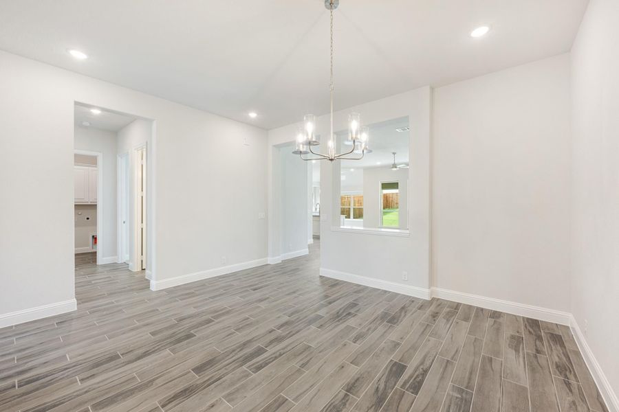 Empty dining room with gray wood-look tile floors, chandelier, and white walls open to hallway