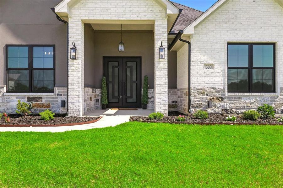 View of exterior entry featuring stone siding, a lawn, and stucco siding View of exterior entry featuring stone siding, a lawn, and stucco siding