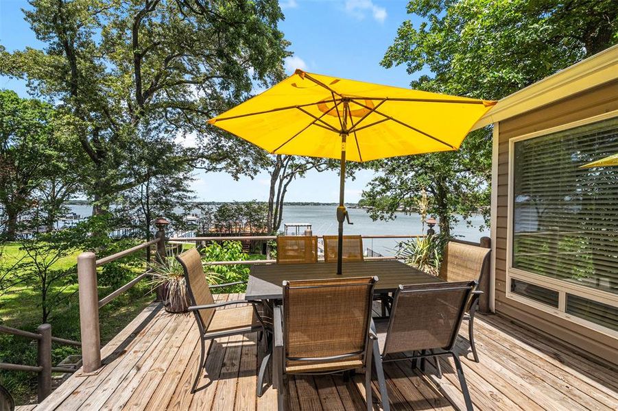 Wood-finish deck with a prominent water backdrop, surrounded by mature trees