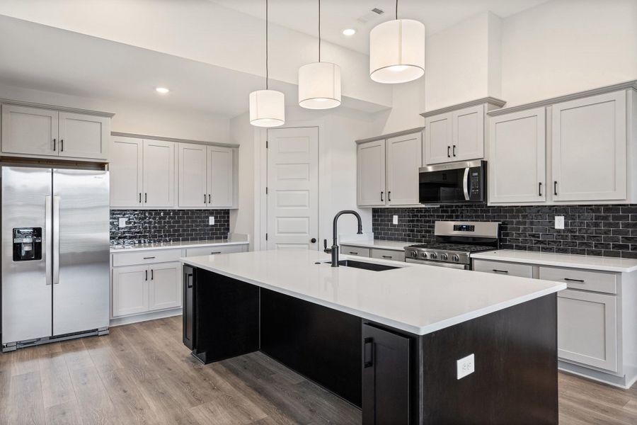 Modern kitchen featuring light gray cabinetry, a central island with a white countertop, and dark subway tile backsplash Modern kitchen featuring light gray cabinetry, a central island with a white countertop, and dark subway tile backsplash