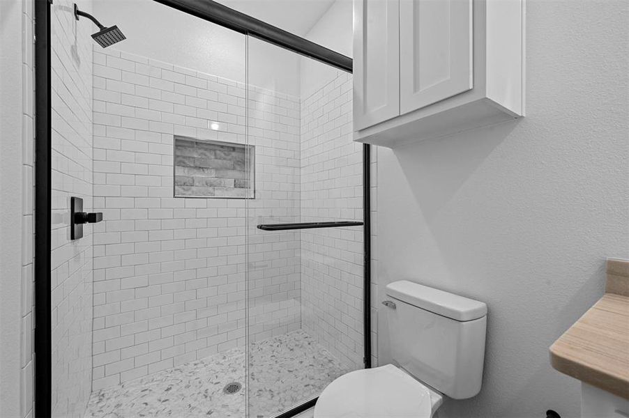 Bathroom featuring a shower with door and toilet