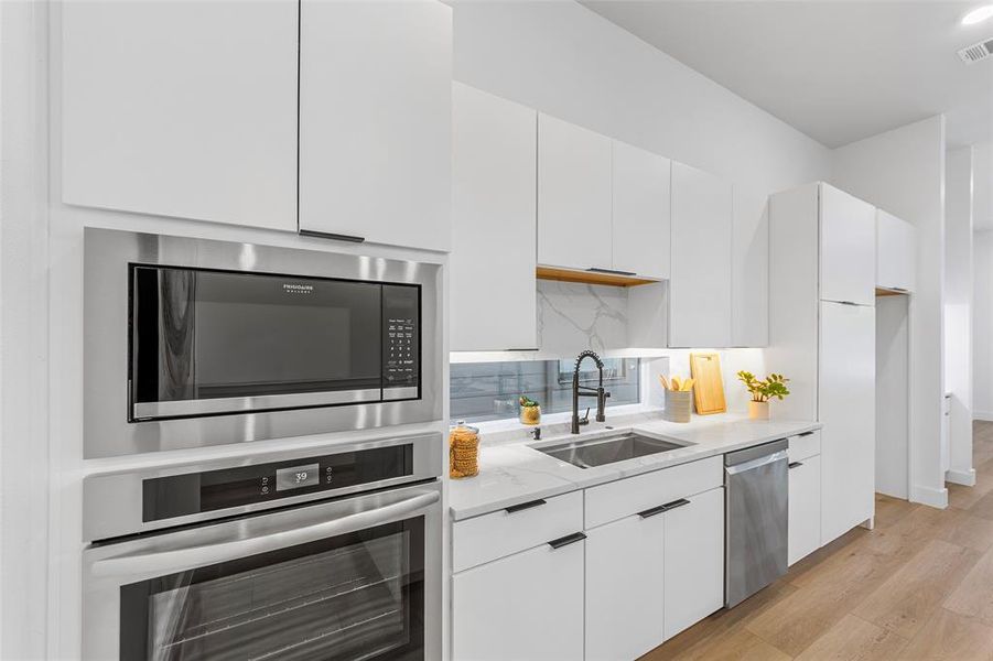 Kitchen with appliances with stainless steel finishes, white cabinets, light wood-style flooring, light stone counters, and modern cabinets Kitchen with appliances with stainless steel finishes, white cabinets, light wood-style flooring, light stone counters, and modern cabinets