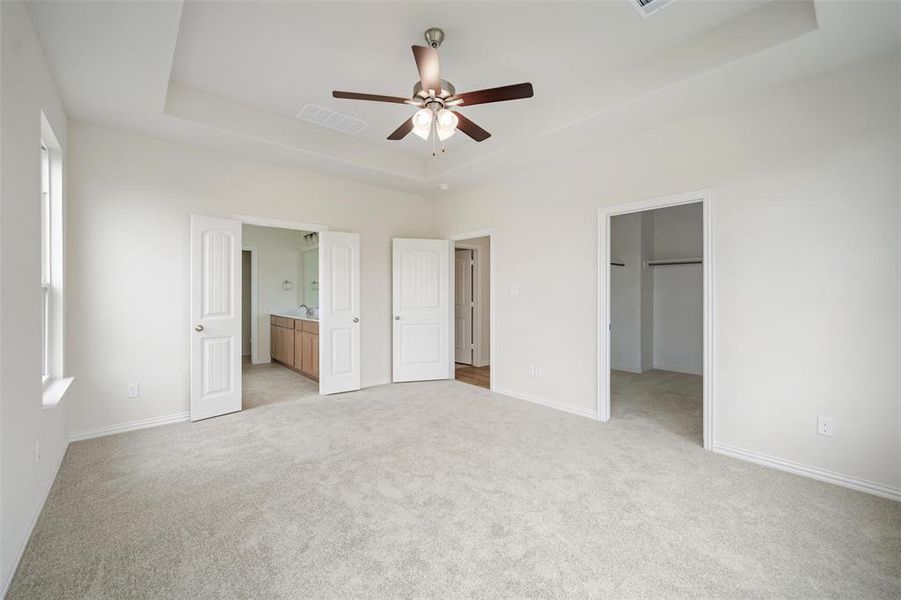 Unfurnished bedroom with a tray ceiling, light colored carpet, a spacious closet, ceiling fan, and connected bathroom