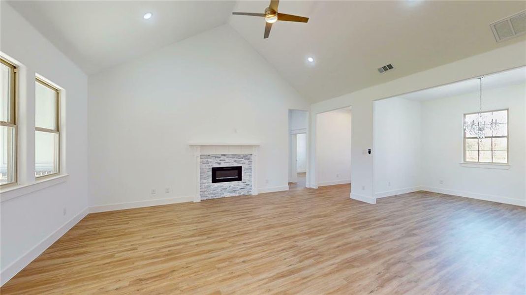 Unfurnished living room featuring ceiling fan with notable chandelier, light wood-style flooring, a fireplace, and visible vents