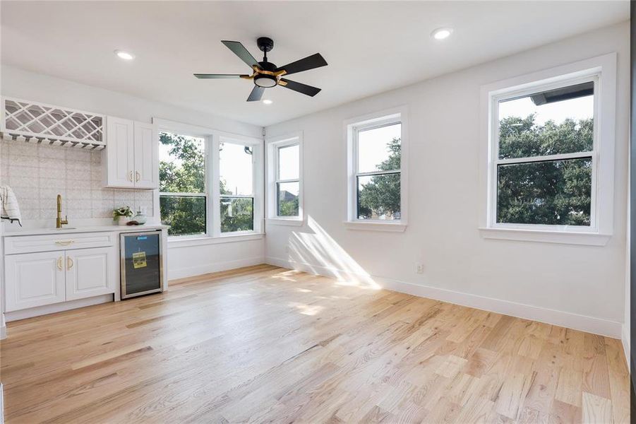 Bar with beverage cooler, light wood-type flooring, decorative backsplash, and white cabinets