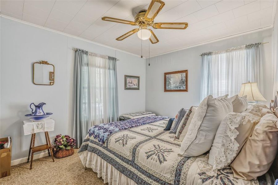 Window with sheer and opaque curtains providing natural light, textured ceiling with a ceiling fan, light-colored walls, and carpet flooring Window with sheer and opaque curtains providing natural light, textured ceiling with a ceiling fan, light-colored walls, and carpet flooring