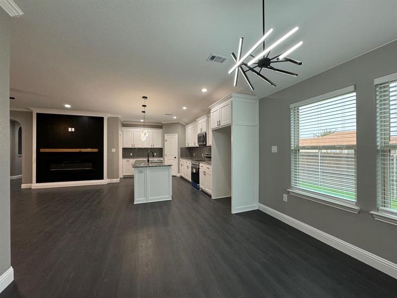 Kitchen with stainless steel appliances, dark wood-type flooring, pendant lighting, a kitchen island with sink, and white cabinets