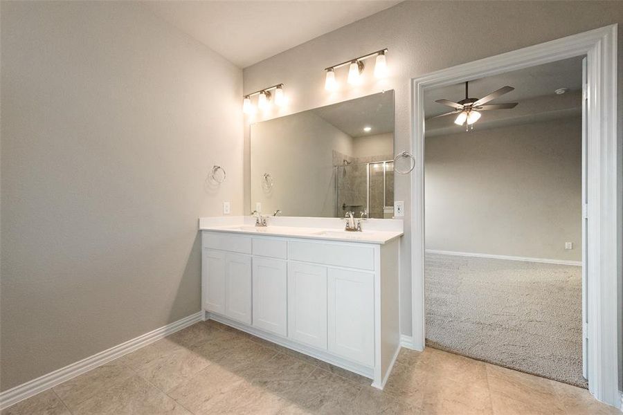 Full bathroom featuring double vanity, a stall shower, ceiling fan, and light colored carpet