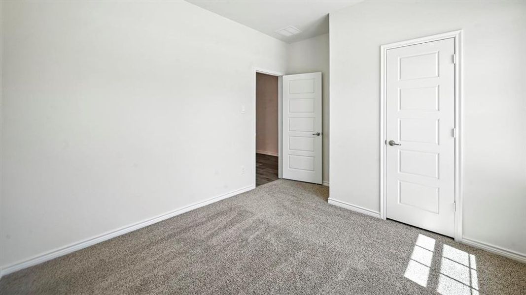 Interior space featuring neutral wall paint, gray carpeting, white baseboards, and a white five-panel interior door Interior space featuring neutral wall paint, gray carpeting, white baseboards, and a white five-panel interior door