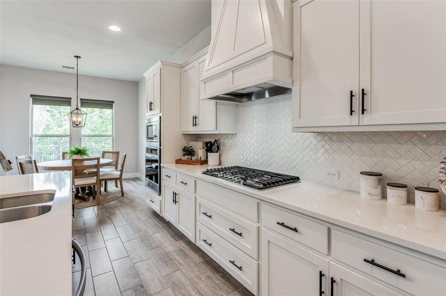 Kitchen featuring tasteful backsplash, stainless steel appliances, white cabinets, premium range hood, and decorative light fixtures