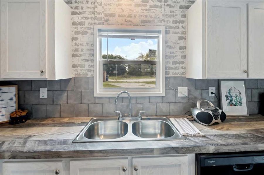 Kitchen with black dishwasher, tasteful backsplash, white cabinetry, and sink