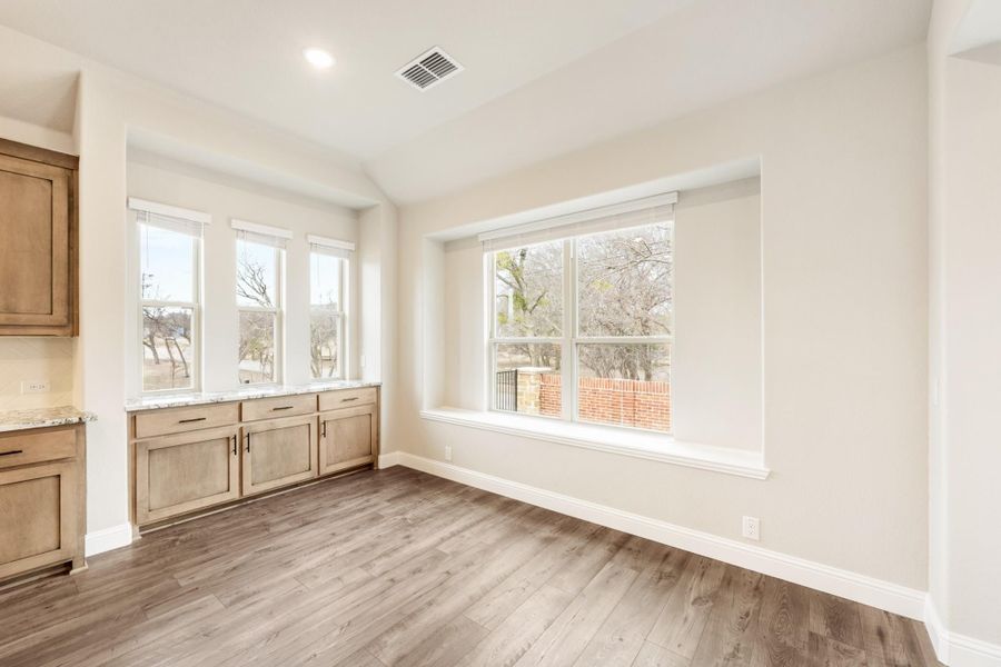 Bright dining area with hardwood floors, wood cabinets, and large windows overlooking trees Bright dining area with hardwood floors, wood cabinets, and large windows overlooking trees
