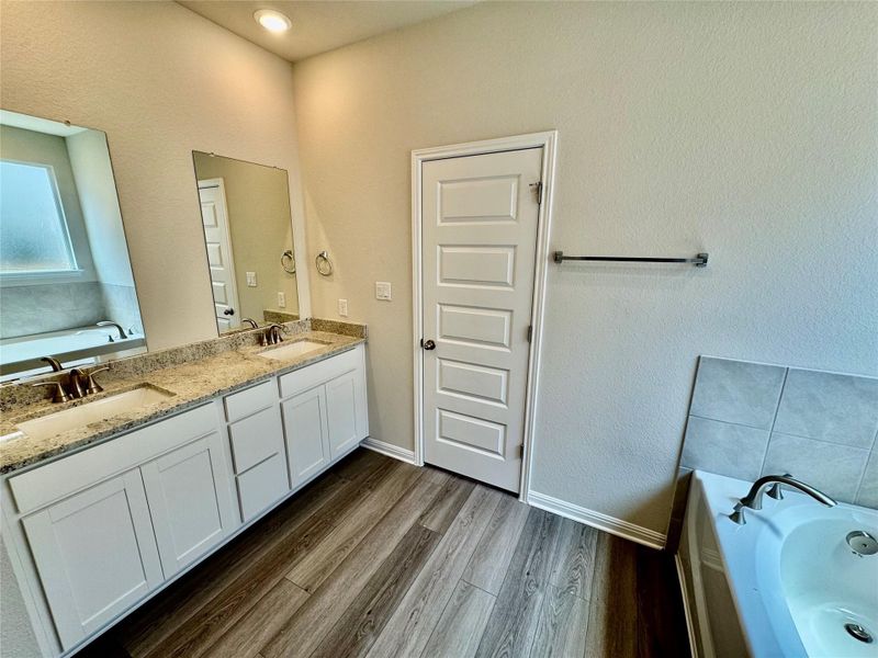 Full bathroom with double vanity, a bath, dark wood-type flooring, and a textured wall Full bathroom with double vanity, a bath, dark wood-type flooring, and a textured wall