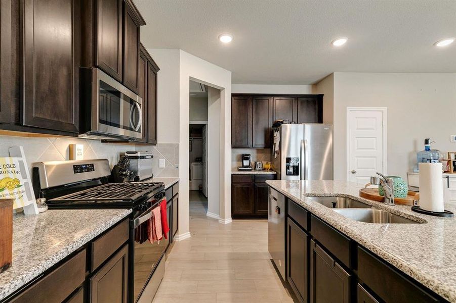 Kitchen with stainless steel appliances, light wood-type flooring, sink, light stone countertops, and backsplash