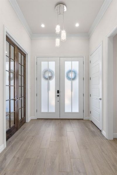 Foyer entrance with french doors, ornamental molding, and light wood-style floors Foyer entrance with french doors, ornamental molding, and light wood-style floors