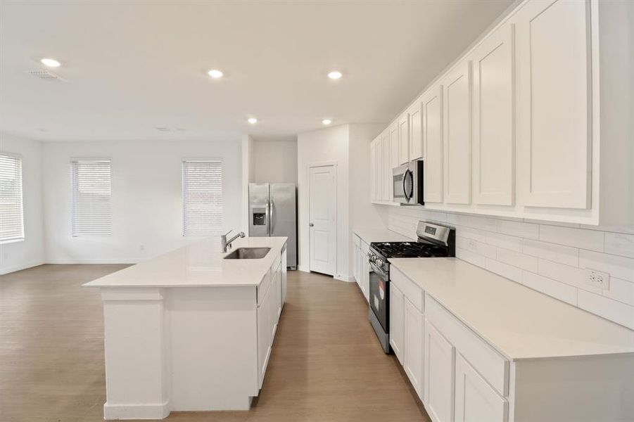 Kitchen with stainless steel appliances, white cabinets, a center island with sink, recessed lighting, and light wood-type flooring