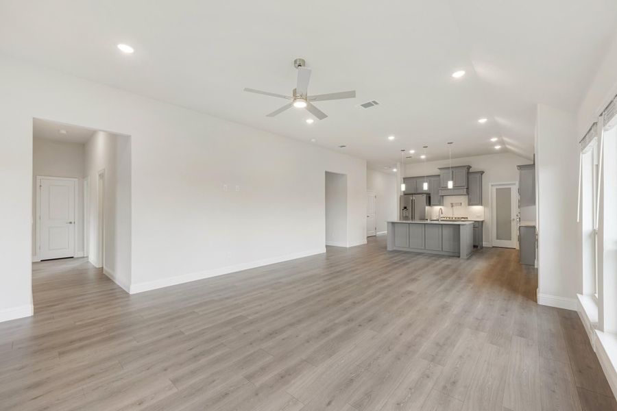 Open living area with wood floors and ceiling fan, open to kitchen with gray cabinets and center island Open living area with wood floors and ceiling fan, open to kitchen with gray cabinets and center island