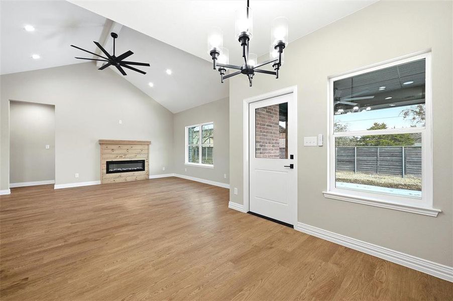 Unfurnished living room with a ceiling fan, light wood-type flooring, a glass covered fireplace, hanging lights, and a high ceiling Unfurnished living room with a ceiling fan, light wood-type flooring, a glass covered fireplace, hanging lights, and a high ceiling