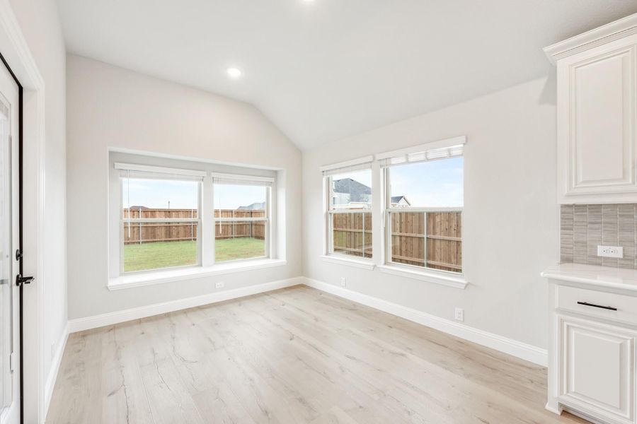 Bright dining area with vaulted ceiling, light wood floors, and large windows overlooking a fenced backyard