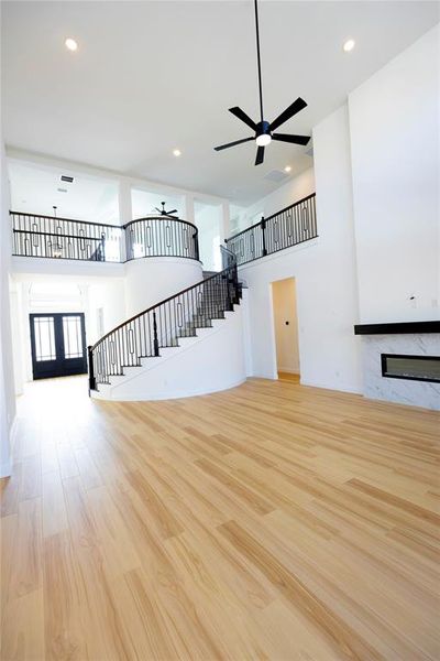 Unfurnished living room featuring a towering ceiling, stairs, light wood-style flooring, recessed lighting, and a high end fireplace Unfurnished living room featuring a towering ceiling, stairs, light wood-style flooring, recessed lighting, and a high end fireplace
