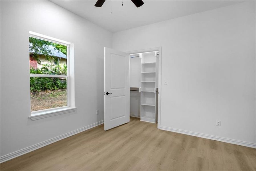 Unfurnished bedroom featuring a walk in closet, light wood-style flooring, and a ceiling fan