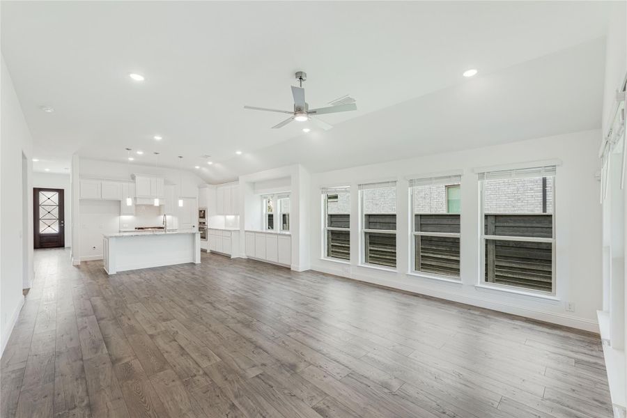 Open-concept living area with hardwood floors, ceiling fan, and white kitchen with island in background Open-concept living area with hardwood floors, ceiling fan, and white kitchen with island in background