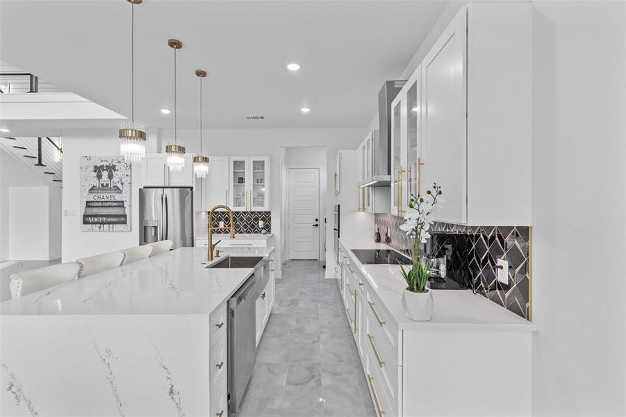 Kitchen with white cabinets, tasteful backsplash, pendant lighting, stainless steel appliances, and a center island with sink