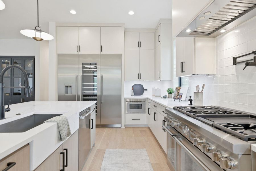 Modern kitchen featuring light wood-finish flooring, white cabinetry with black hardware, stainless steel appliances, and white countertops