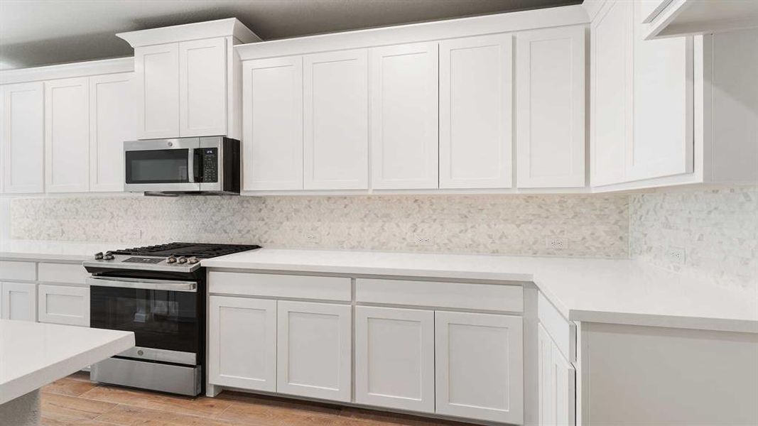 Kitchen with light hardwood / wood-style flooring, white cabinetry, backsplash, and stainless steel appliances