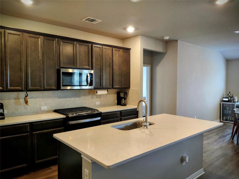 Kitchen featuring dark brown cabinets, range with gas stovetop, stainless steel microwave, and light stone countertops